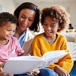 Mother sitting on sofa in the living room with her children, reading them a book