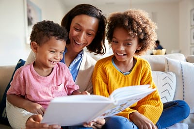 Mother sitting on sofa in the living room with her children, reading them a book Mother sitting on sofa in the living room with her children, reading them a book