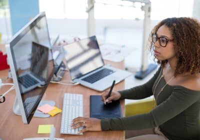 Female graphic designer working on computer while using graphic tablet at desk