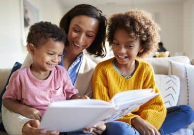 Mother sitting on sofa in the living room with her children, reading them a book