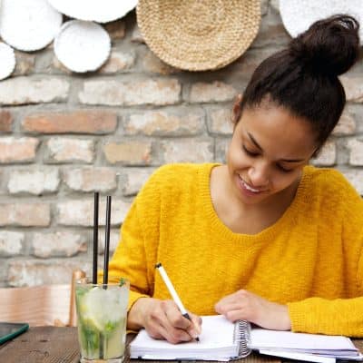 Beautiful young black woman writing notes at cafe